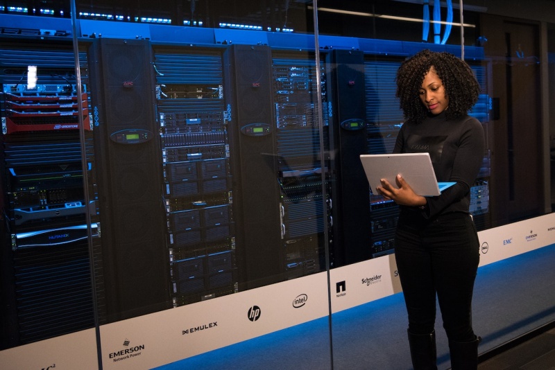 A woman standing next to a server rack, holding a laptop
